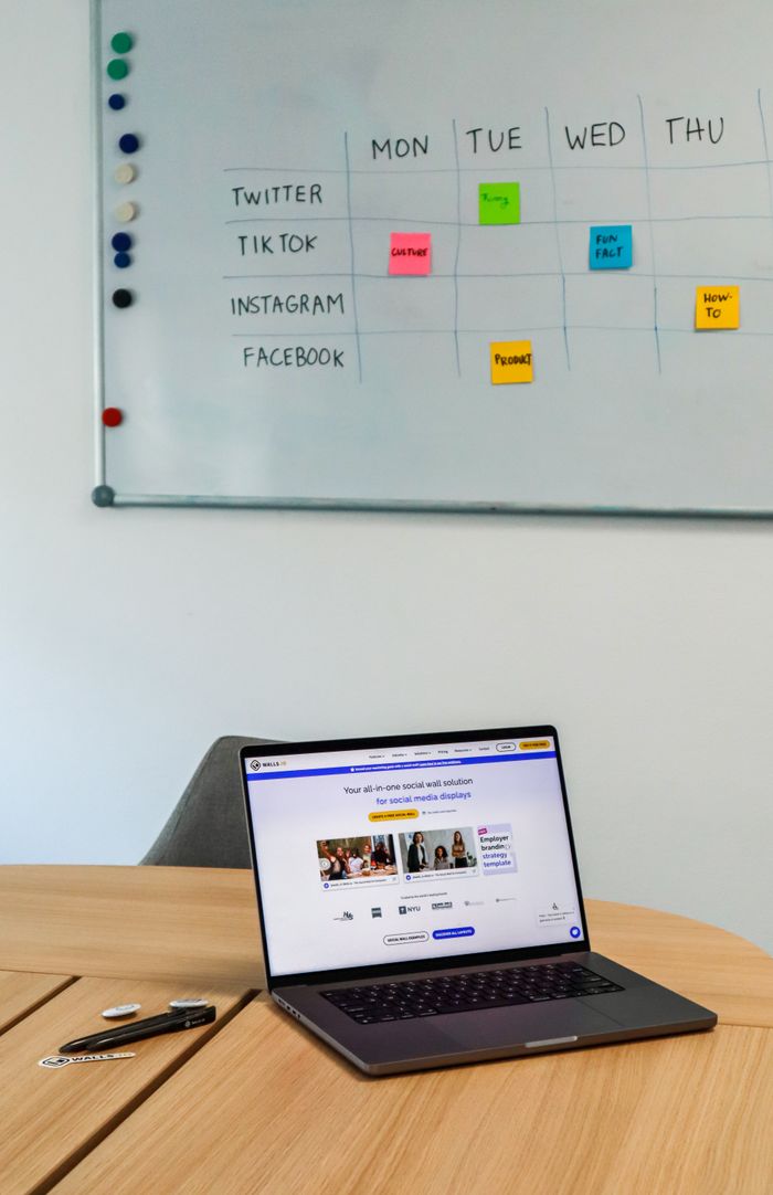 A contemporary office arrangement showcasing a laptop alongside a whiteboard schedule for social media platforms.